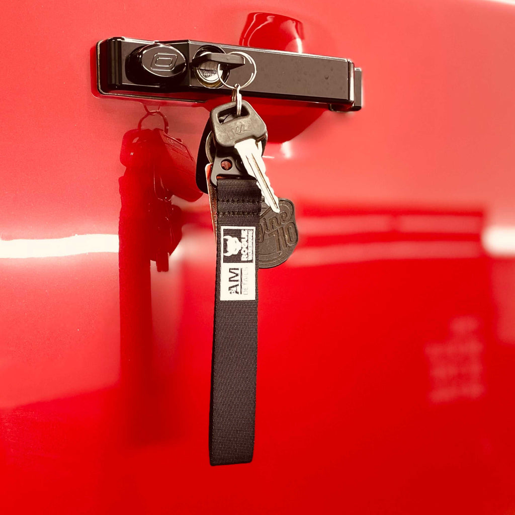 A close-up image of a red Land Rover Defender  black door handle with an optimal handle. A prominent feature in the picture is a keychain with a red warehouse key clipped onto the door handle.